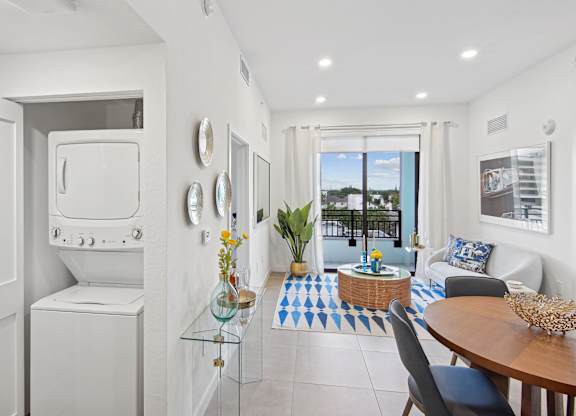 A modern living room with a dining table and chairs and a washer and dryer on the left at Hollywood Heights on the Boulevard Luxury Apartments in Hollywood, FL