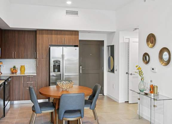 A modern kitchen with a dining table and chairs, fridge with a ice maker, stovetop, and microwave  Living room and modern kitchen in our 2-bedroom model with a dining table and chairs  Balcony view of Hollywood Boulevard at Hollywood Heights on the Boulevard Luxury Apartments in Hollywood, FL