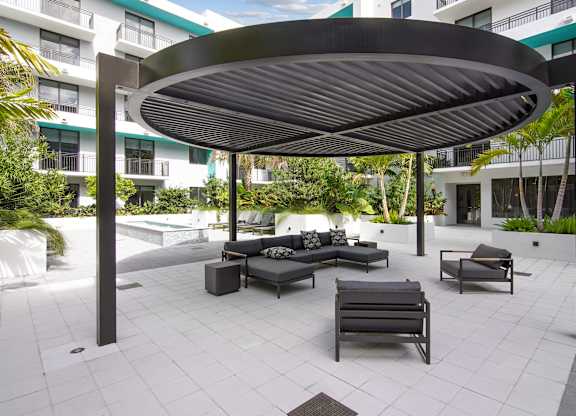 A patio with cushioned outdoor seating under a circular pergola at our courtyard at Hollywood Heights on the Boulevard Luxury Apartments in Hollywood, FL