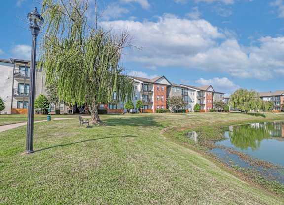 A serene pond with benches and apartment buildings in the background at Ultris Island Park in Shreveport, LA