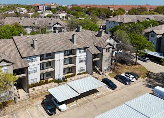 An apartment building with a parking lot and covered parking spots at Jefferson Place Apartments in Irving, TX