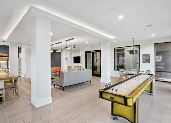 A shuffleboard table is in the middle of a spacious entertainment lounge with sofas and white walls at Knox Heights Apartments in Dallas, TX