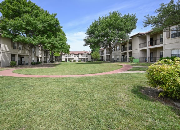 a grassy area with trees and apartment buildings in the background