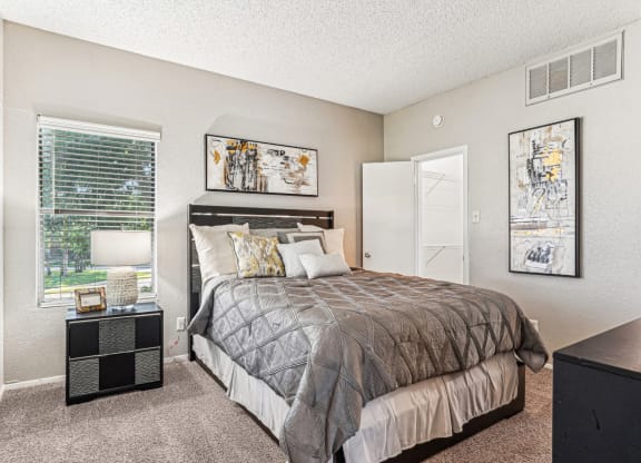Comfortable bedroom with a grey upholstered bed and neutral decor at Laurels of Sendera apartments in Arlington, TX
