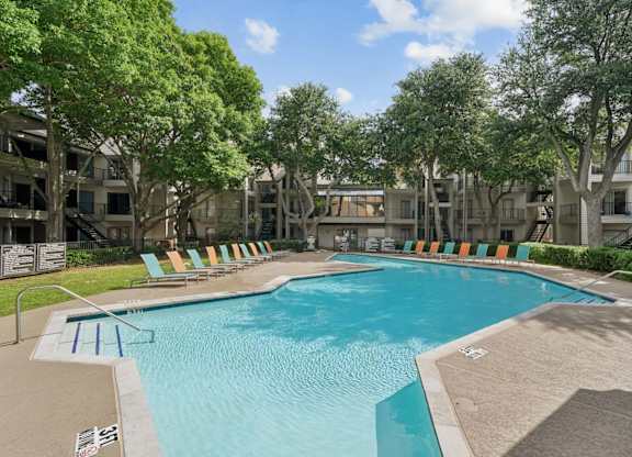 A swimming pool surrounded by trees and chairs.