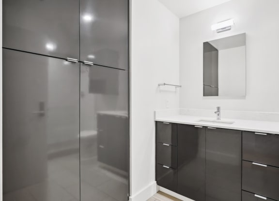 Sleek bathroom with walk-in shower, modern vanity with white countertop and black cabinets at Mid Elm Lofts in Dallas, TX