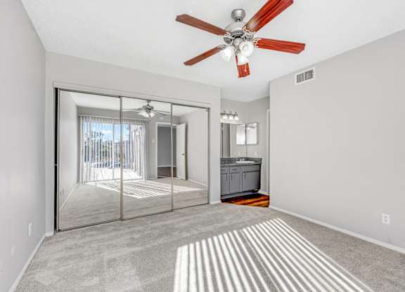 A bedroom with a ceiling fan and a closet with sliding mirrored doors at Montfort Crossing Apartments in Dallas, TX.