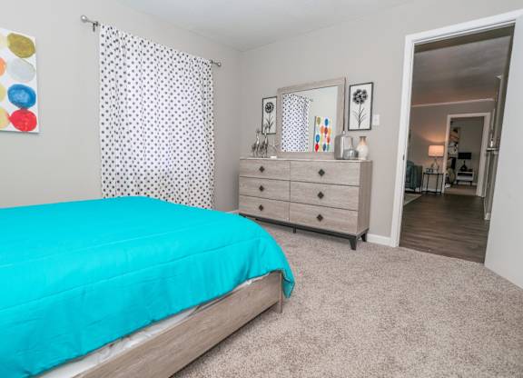 A cypress bedroom with a teal bedspread and a white dresser with mirror at The Marq in Shreveport, LA
