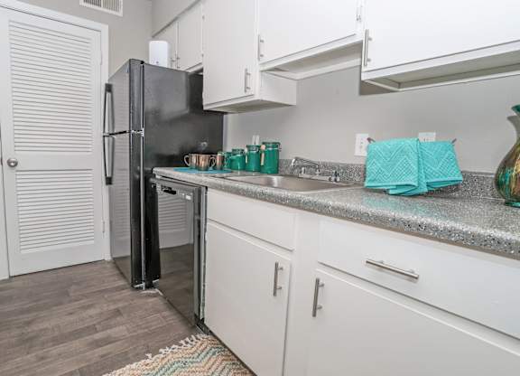 A black refrigerator is in a cypress kitchen with white cabinets at The Marq in Shreveport, LA