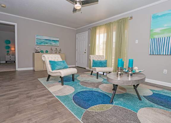 A cypress living room with a blue and white rug, a white chair, and a painting of a beach scene on the wall at The Marq in Shreveport, LA