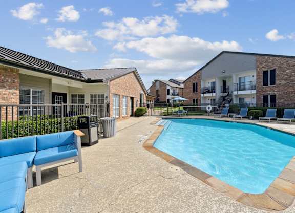 A pool with comfortable lounge chairs and a bench at The Oaks of Denton Apartments in Denton, TX