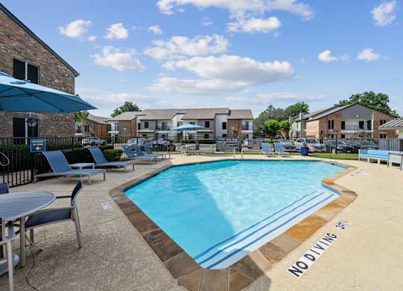 A pool surrounded by comfortable blue lounge chairs at The Oaks of Denton Apartments in Denton, TX