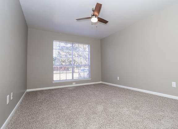 A bedroom with a ceiling fan, large window, and lush carpet at Orleans Square in Shreveport, LA