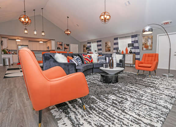 A clubhouse room with a black and white rug, orange chairs, and a kitchen area in the background at Orleans Square in Shreveport, LA