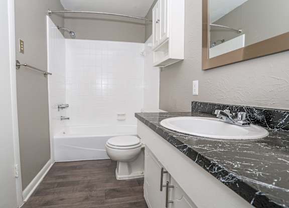 A bathroom with a marble counter, toilet, sink, and tub at Orleans Square in Shreveport, LA