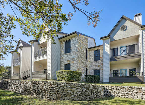 Our apartment buildings with balconies and a stone wall at On the Green apartments in Austin, TX
