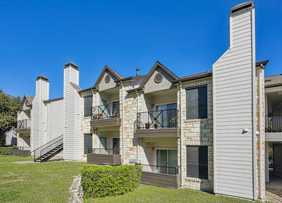 Row of our apartment buildings with balconies and a clear blue sky at On the Green apartments in Austin, TX