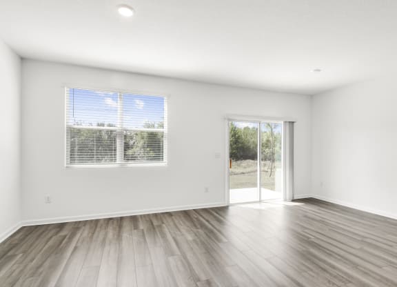 a spacious living room with white walls and hardwood floors