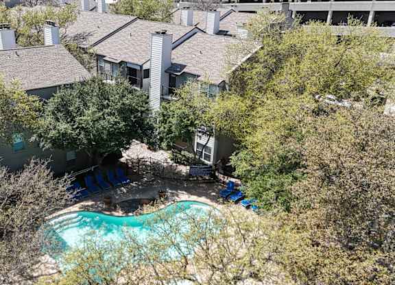 A swimming pool surrounded by lush trees and apartment buildings at The Park on Preston Apartments in Dallas, TX