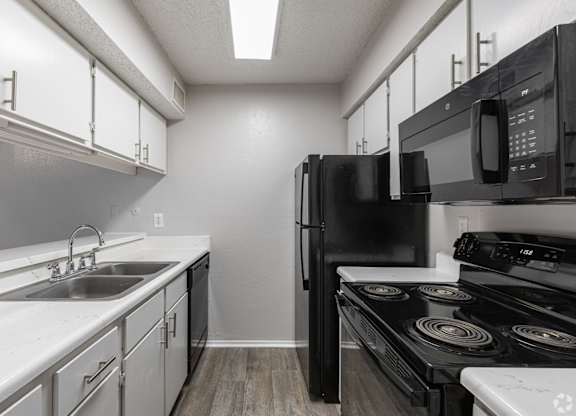 A kitchen with black appliances and white cabinets at Preston Oaks Apartments in Dallas, TX.