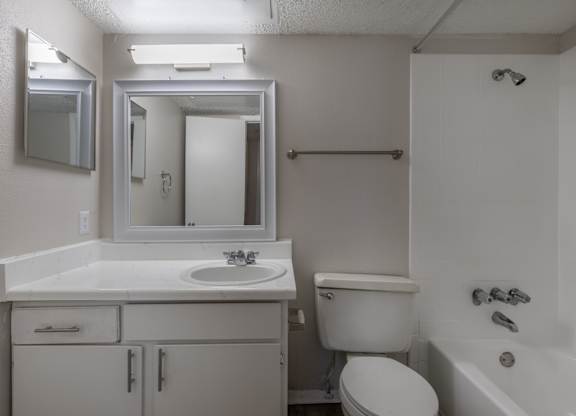 A white bathroom with a sink, toilet, and bathtub at Preston Oaks Apartments in Dallas, TX.