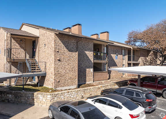 A stone apartment building with a parking lot in front at Preston Oaks Apartments in Dallas, TX.