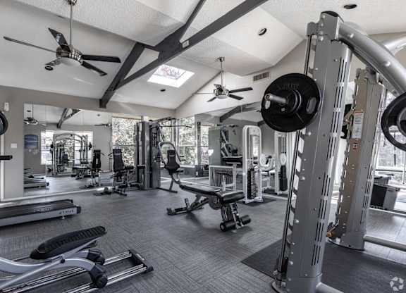 A gym with a variety of equipment including a weight bench, a barbell, and a squat rack at Preston Oaks Apartments in Dallas, TX.