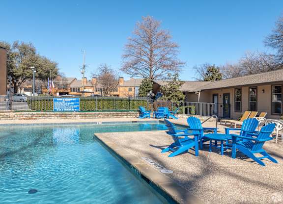 A pool with blue chairs a blue sky in the background at Preston Oaks Apartments in Dallas, TX.