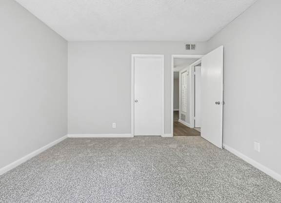 First bedroom with a carpeted floor and a closet door in B1 floor plan at Riverwood Crossing apartments in Roswell, GA.