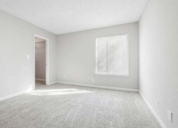 First bedroom with a carpeted floor, a window with blinds, and walk-in closet in the B1 floor plan at Riverwood Crossing apartments in Roswell, GA..