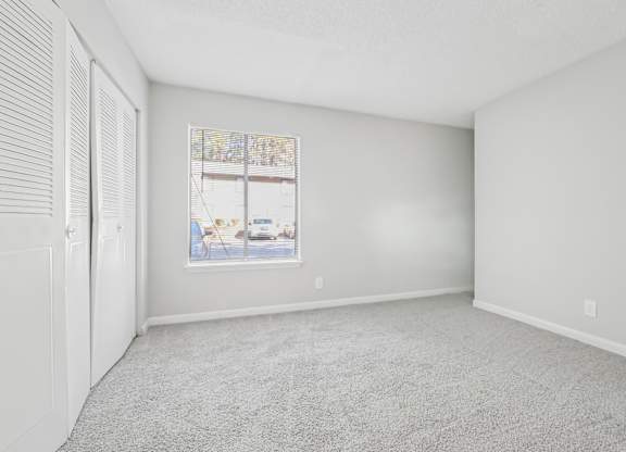 Second bedroom with a carpeted floor and a large window in B1 floor plan at Riverwood Crossing apartments in Roswell, GA.