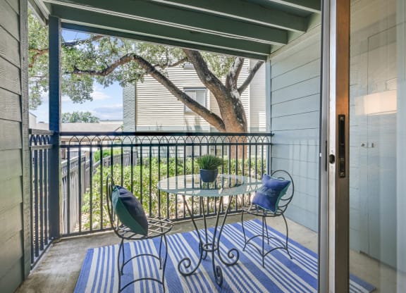 a small table and two chairs sit on a striped rug on a balcony with a sliding glass