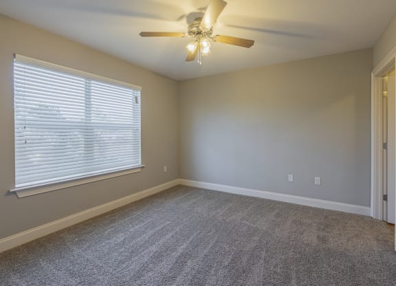 an empty living room with a large window and a ceiling fan