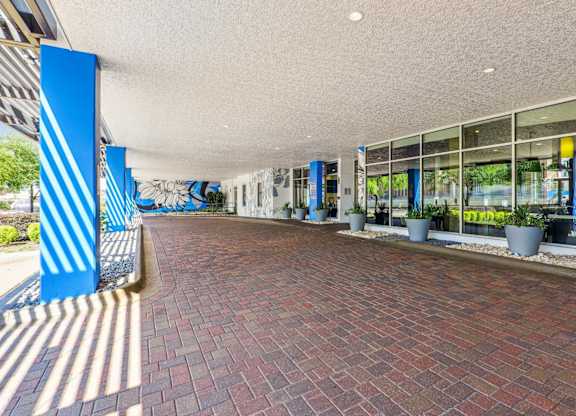 A covered entrance to The Grand at Upper Kirby with a brick road and glass windows in Houston, TX
