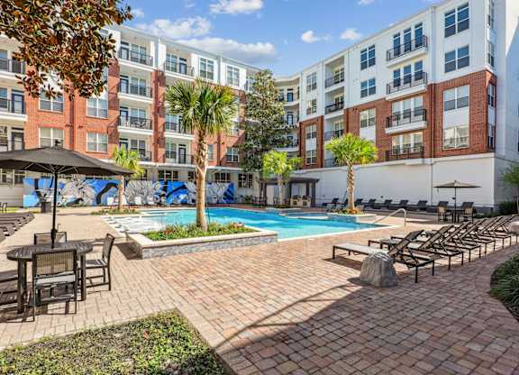 A courtyard pool area with lounge chairs and palm trees at The Grand At Upper Kirby in Houston, TX