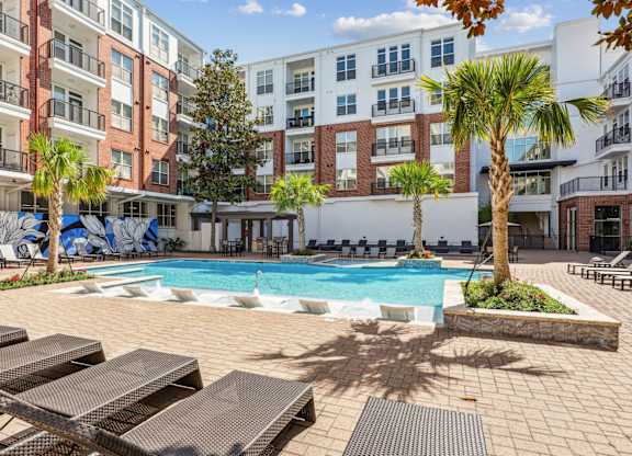 A pool surrounded by lounge chairs and palm trees at The Grand At Upper Kirby in Houston, TX