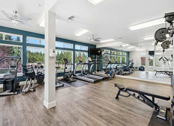 A gym with a variety of equipment including treadmills, weights, and a bench at The Madison apartments in Olympia, WA