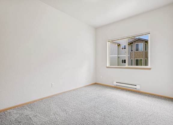 A bedroom with a carpeted floor and a window showing the apartment complex outside at The Madison Apartments in Olympia, WA