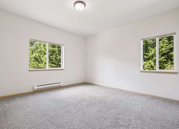 A bedroom with a carpeted floor and two windows at The Madison Apartments in Olympia, WA