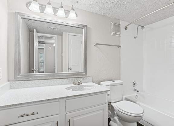 Upgraded A1 white bathroom with a toilet, sink, and mirror at Vine Apartments in Arlington, TX