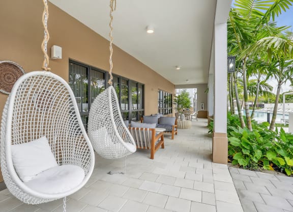 a seating area with hanging chairs and a pool in the background at Westgate on Univeristy in Lauderhill, FL