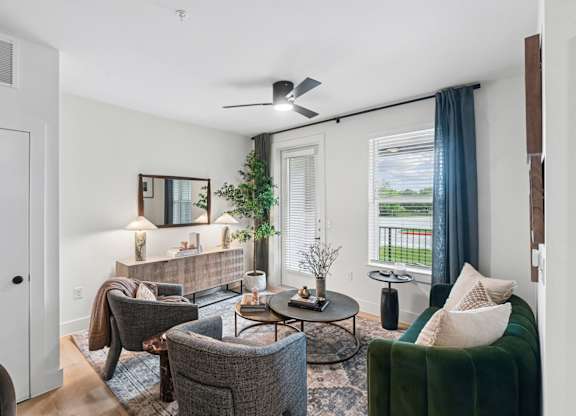 Model living room with a grey couch, a green couch, a coffee table, and a ceiling fan at Whispering Pines at Westdale Hills in Euless, TX
