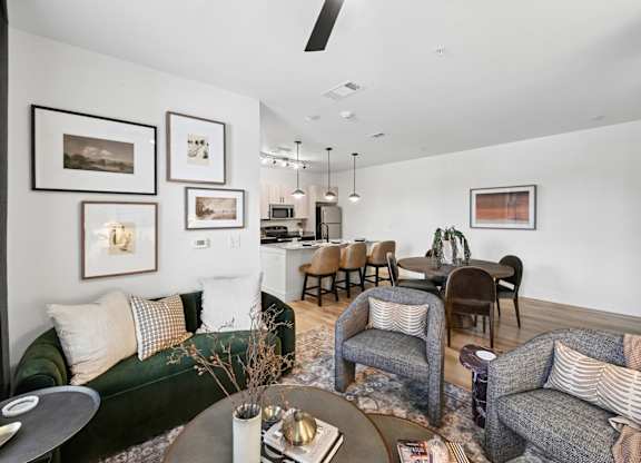Model apartment living room with a green couch, a grey couch, a coffee table, and a dining table with chairs at Whispering Pines at Westdale Hills in Euless, TX