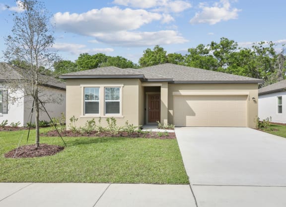 a home with a concrete driveway and a tree in the front yard at Beacon at Woodland Village, Florida