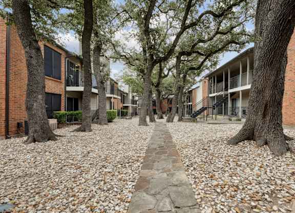 Stone walkway surrounded by trees and apartment buildings at Westdale Pointe in Austin, TX