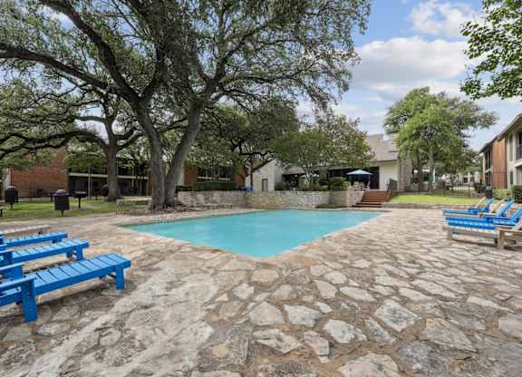 A pool surrounded by trees and chairs.