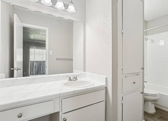A6 bathroom with a sink, mirror, towel closet, and toilet Windridge on the Parkway apartments in Dallas, TX.