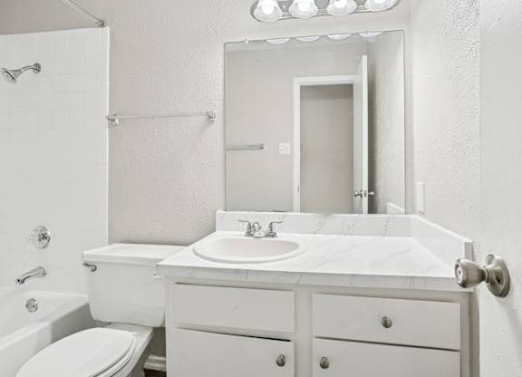 B6 white bathroom with a toilet, sink, and mirror at Windridge on the Parkway in Dallas, TX