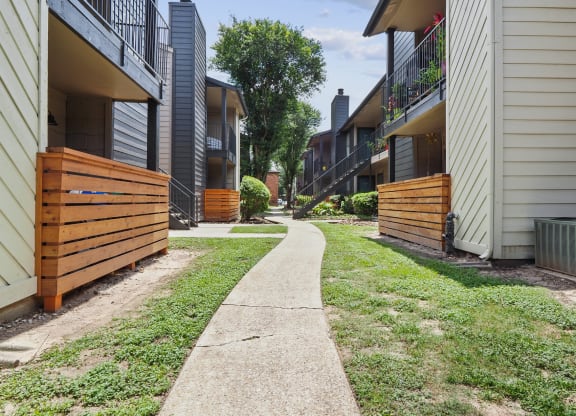 a path between two buildings with a wood fence on the left and a brick building on the