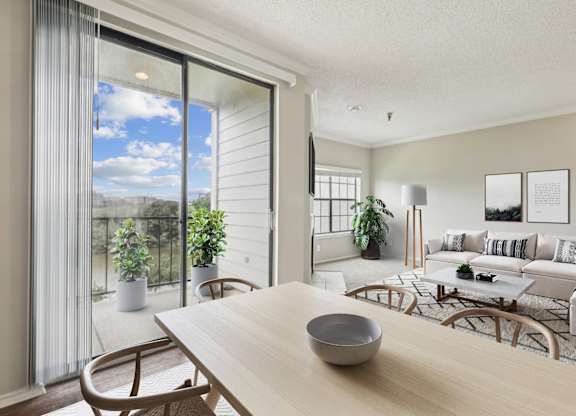 A modern living room  in the A2 floorplan with a wooden table and chairs and a glass sliding door leading to the balcony at Jefferson Creek Apartments in Irving, TX